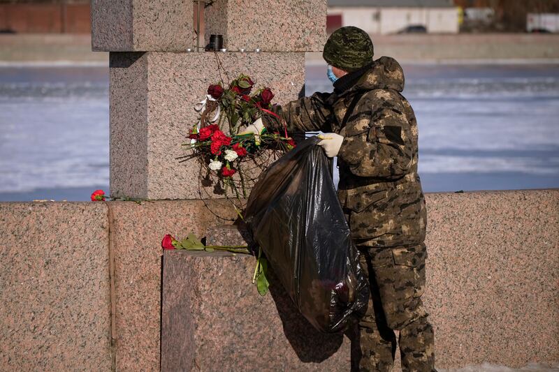 A municipal worker, on orders from the authorities, removes flowers brought by people to pay respects to Alexei Navalny from the Memorial to Victims of Political Repression in St Petersburg, Russia (Dmitri Lovetsky/AP)