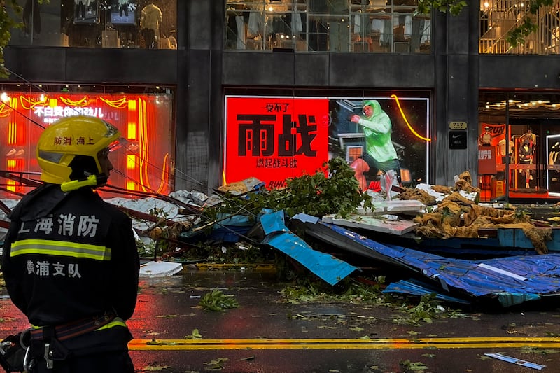 A firefighter stands near debris on a business street in Shanghai, China, in the aftermath of Typhoon Bebinca (Chinatopix Via AP)