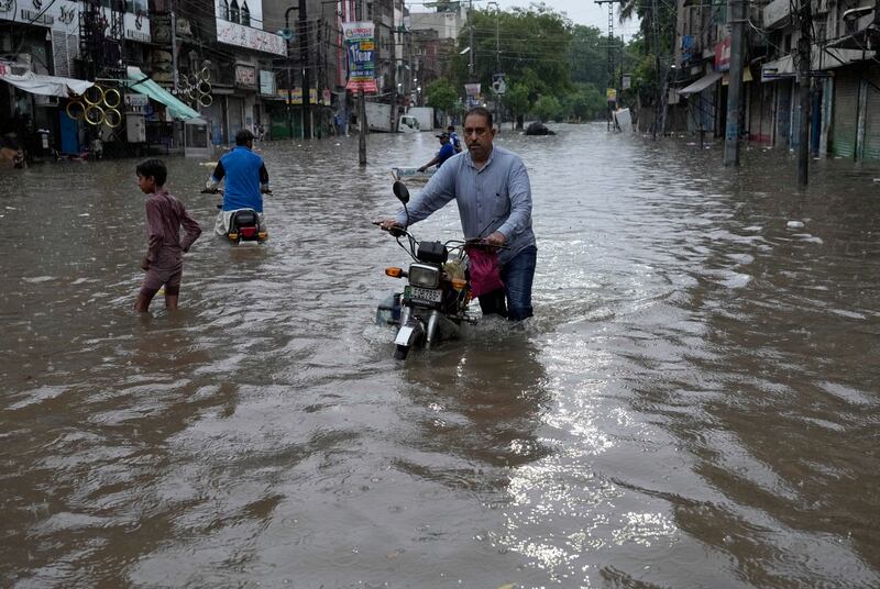 Motorcyclists drive through a flooded road caused by heavy monsoon rainfall in Lahore, Pakistan (KM Chaudary/AP)