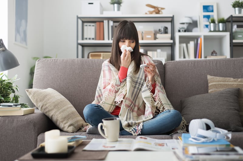 Sick woman sat on a sofa measuring her temperature with a thermometer