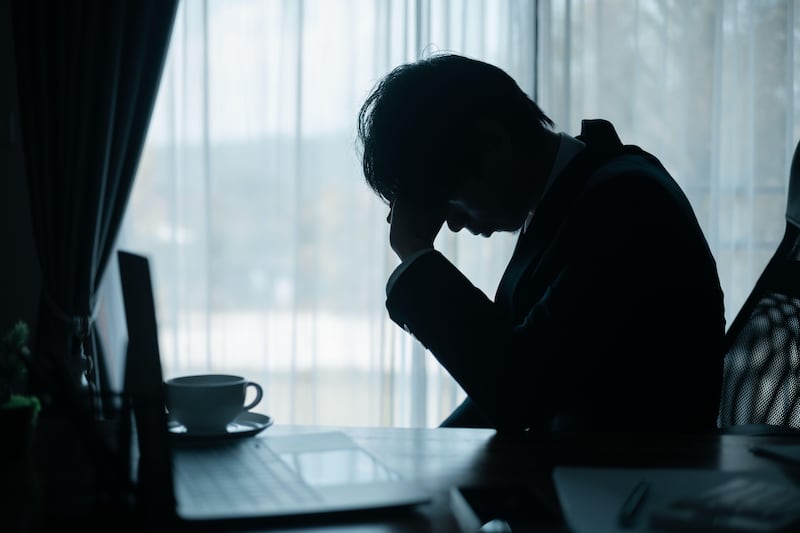 Shadow of stressed businessman sat at his desk in a dark office