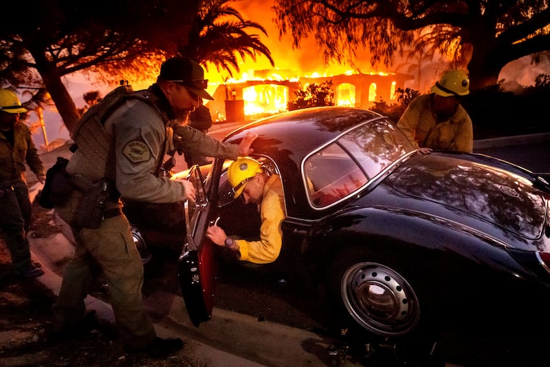 Firefighters and sheriff’s deputies push a vintage MG away from a burning home as the Mountain Fire burns in Camarillo, California (Noah Berger/AP)