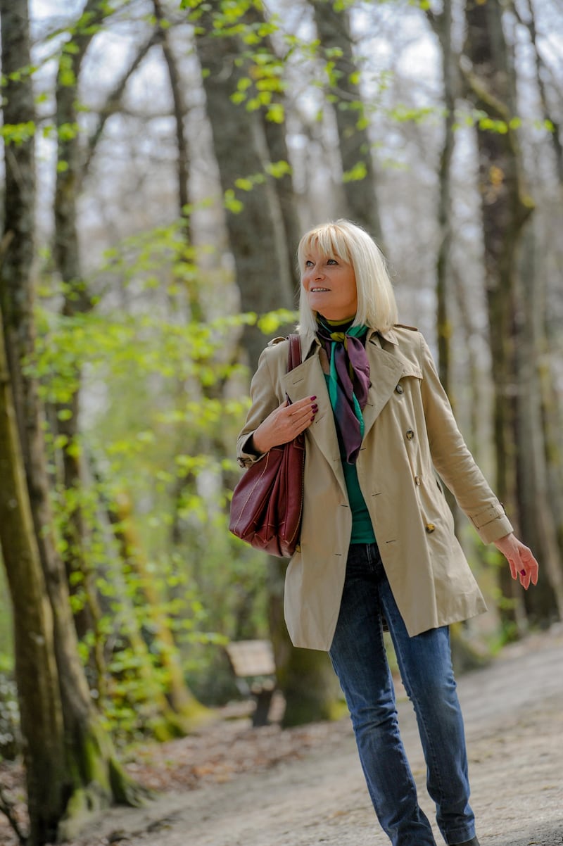 Senior woman wearing a beige coat smiling and strolling around a park