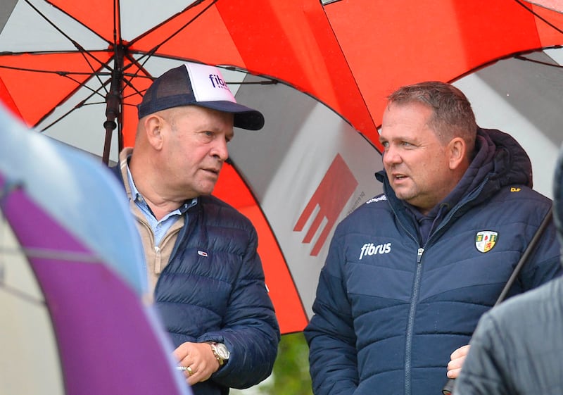 Two men wearing Antrim jackets and holding umbrellas