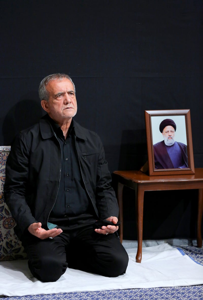 Iran’s President-elect Masoud Pezeshkian prays next to a portrait of the late President Ebrahim Raisi (Office of the Iranian Supreme Leader/AP)