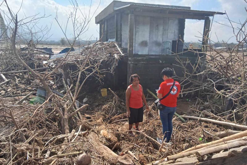 A volunteer talks to a resident beside damaged trees and debris swept by floods caused by Typhoon Usagi in 2024. (Philippine Red Cross via AP)