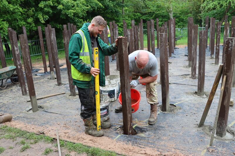 Workers refurbish the wooden posts at the memorial