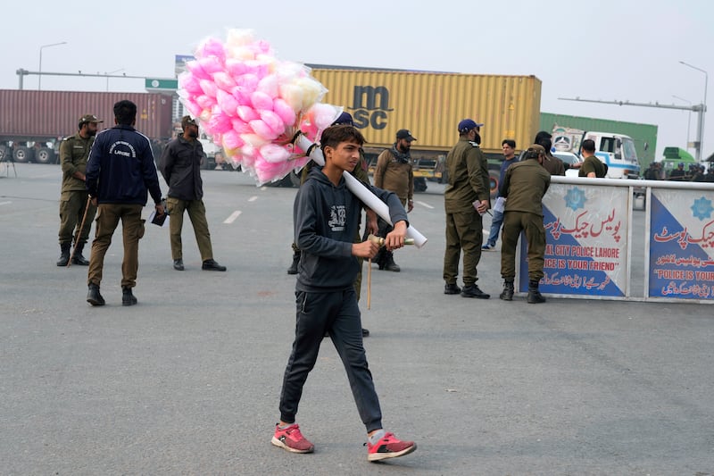 A cotton candy seller walks past police officers standing guard on an entry point to the motorway leading to Islamabad (KM Chaudary/AP)