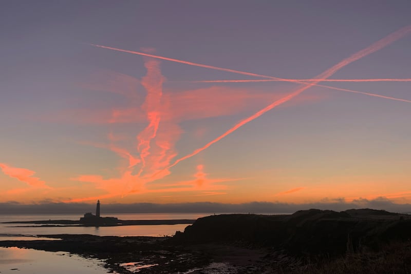 Plane contrails lit by the sun below the horizon before sunrise at St Marys Lighthouse in Whitley Bay off the North East coast