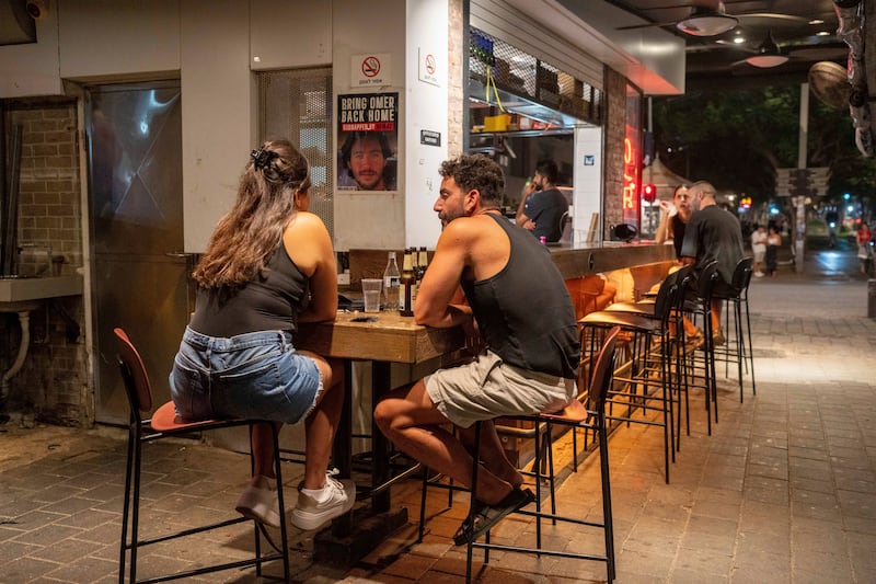 People sit in a bar near a sign calling for the release of hostages held by Hamas (AP Photo/Ohad Zwigenberg)