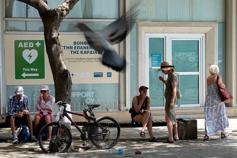 People sit under a tree for shade amid hot weather in a square in Nicosia (Petros Karadjias/AP)