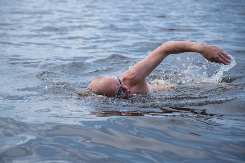 An elderly man swimming in a lake while wearing goggles