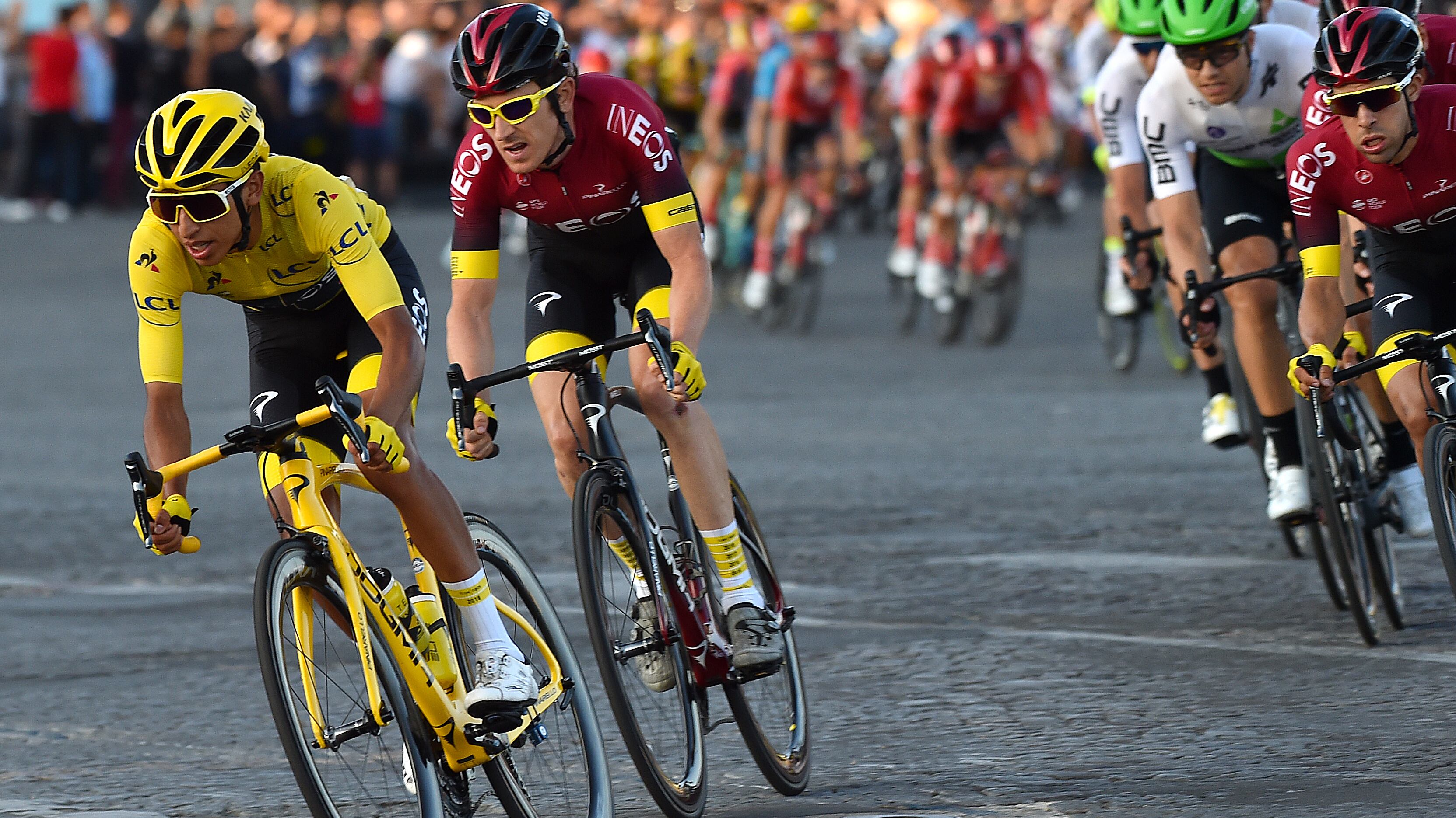 A shot from the Tour de France stage 21 in 2019, a cyclist in a yellow jacket and two cyclists in maroon jackets