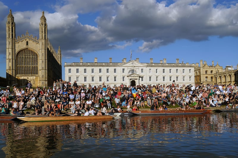 People sit on the banks of the River Cam, in punts on the water and on the lawns of King’s College in Cambridge, as they listen to The King’s Men perform