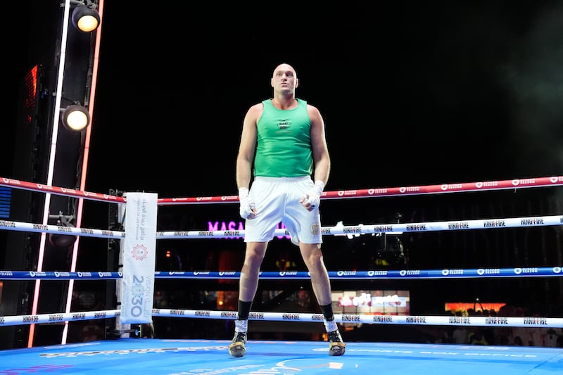 Tyson Fury standing in a boxing ring wearing white shorts and a hand wrap and a green vest during his open workout