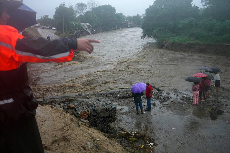 Residents stand alongside the banks of a river on the outskirts of San Pedro Sula, Honduras (Moises Castillo/AP)