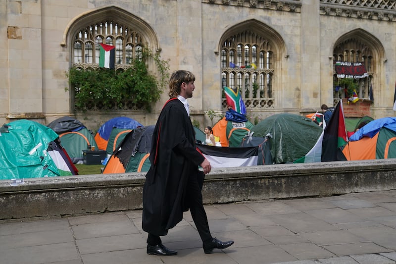 A graduating student walks past the Gaza protest encampment at Cambridge University