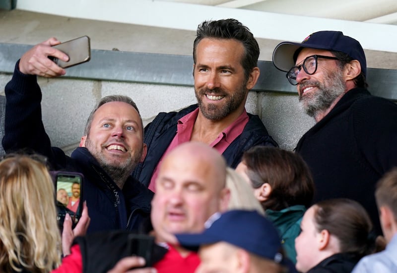 Hollywood actor Hugh Jackman (right) and Ryan Reynolds pose for a photo with a fan at a Wrexham game