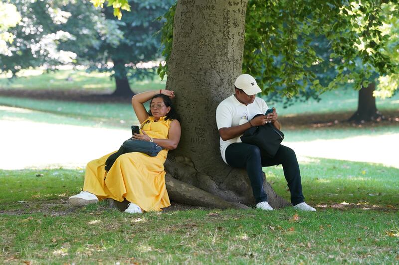 People sit in the shade beneath a tree during hot weather in St James’s Park, central London