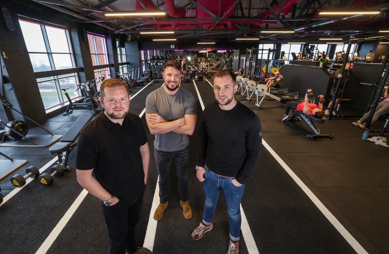 Three men standing on a running track in a gym.