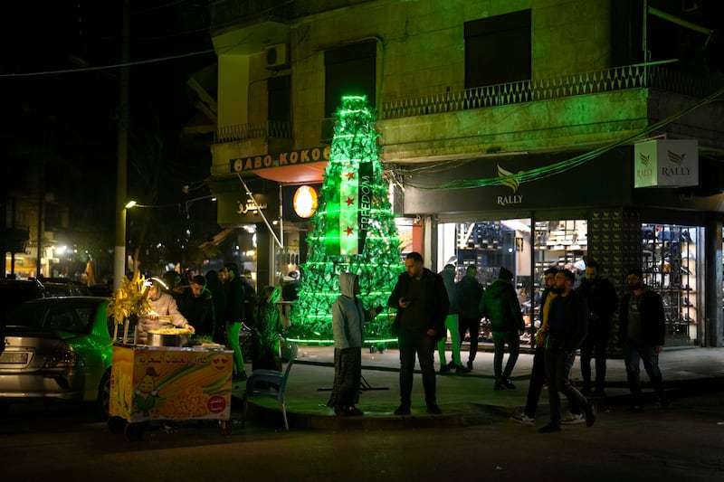 People stand next to a illuminated Christmas tree decorated with the ‘revolutionary’ Syrian flag in the city of Aleppo (Khalil Hamra/AP)