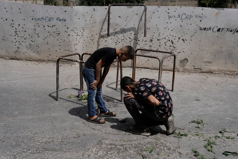 Palestinians next to a wall damaged from shrapnel, after a military operation in Zababdeh (Majdi Mohammed/AP)