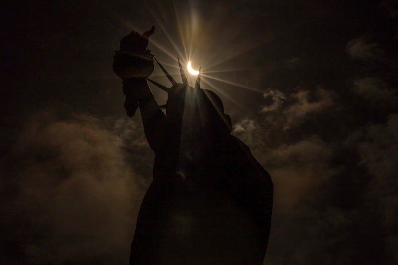 The moon partially covers the sun behind the Statue of Liberty in New York during the solar eclipse (Yuki Iwamura/AP)