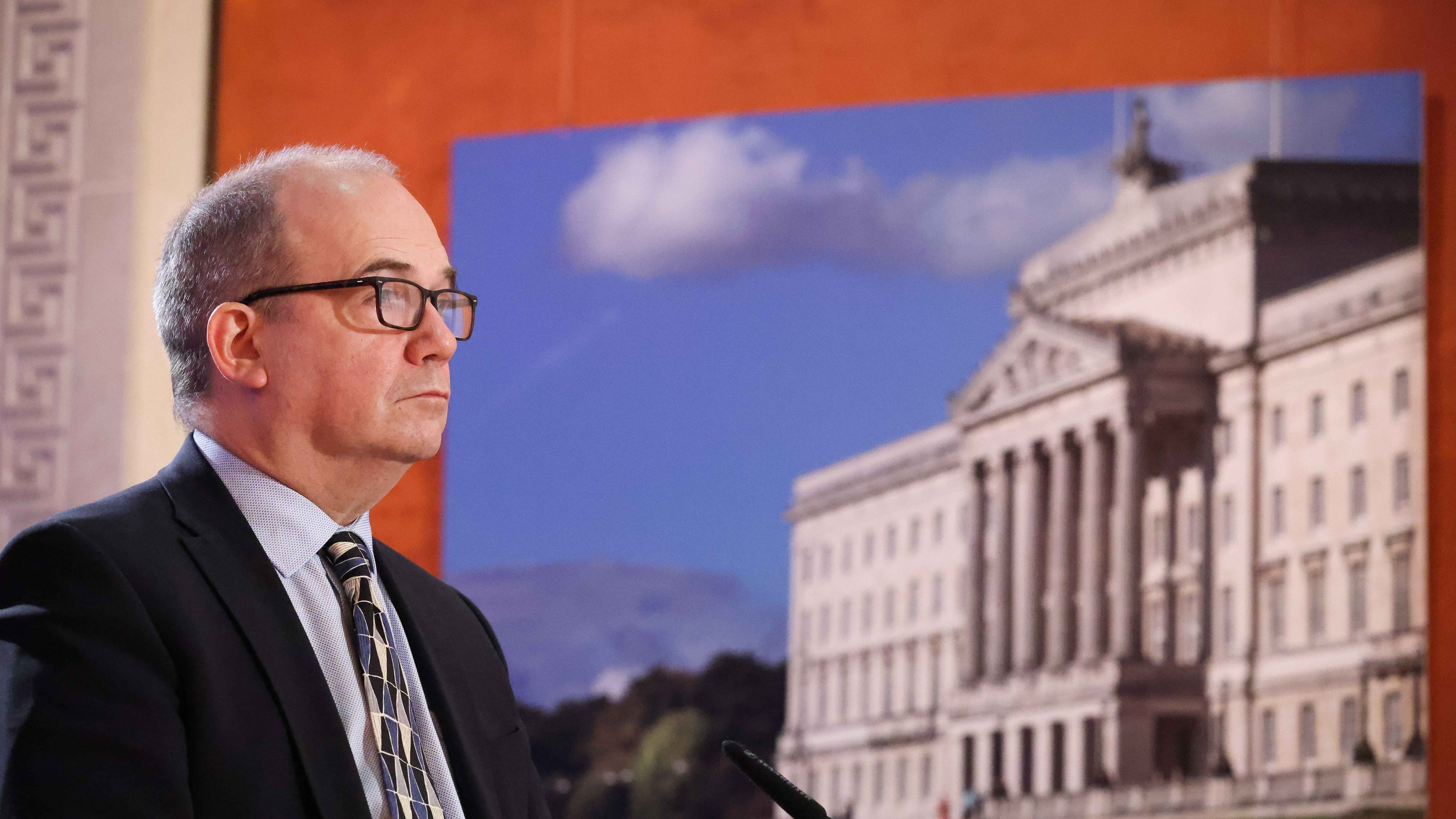 Chief Medical Officer Dr Michael McBride beside a picture of parliament buildings, stormont