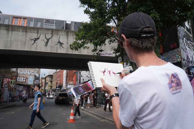 A person draws a new artwork depicting three monkeys unveiled by Banksy