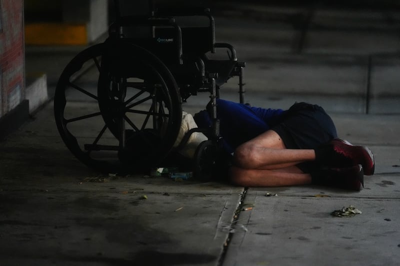 A homeless person sleeps under a wheelchair alongside a parking garage in deserted downtown Tampa, Florida (Rebecca Blackwell/AP)