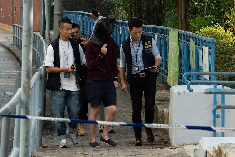 An unidentified person wearing a hood is escorted by police to the park where the body was found for a video reconstruction (Bertha Wang/AP)