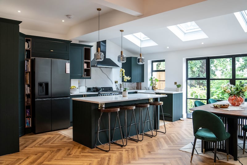 An open-plan transitional kitchen features premium dark green cabinetry