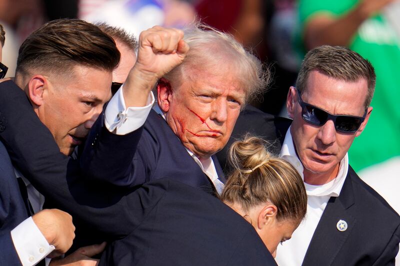 Former president Donald Trump pumps his fist as he is helped off the stage by US Secret Service agents (Gene J Puskar/AP)