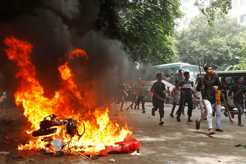 Men run past a burning vehicle inside the Bangabandhu Sheikh Mujib Medical University Hospital, set on fire by protesters during a rally against Sheikh Hasina (AP)