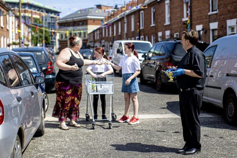 Irene Leckey (left) with her granddaughters Meabh Connolly (second left) and Grace Connolly (centre) stand helping Fr Tim Bartlett of St Mary's Church in Belfast to give out Holy Water on Hamill Street during Pentecost Sunday. Picture by Liam McBurney, Press Association