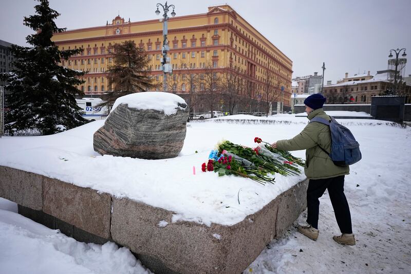 A woman lays flowers at the monument where the first camp of the Gulag political prison system was established, with the Federal Security Service (FSB, Soviet KGB successor) building in the background, in Moscow (Alexander Zemlianichenko/AP)