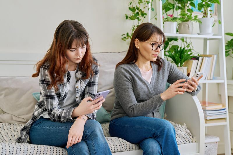 Mother and teenage daughter both sat on the sofa looking at their phones