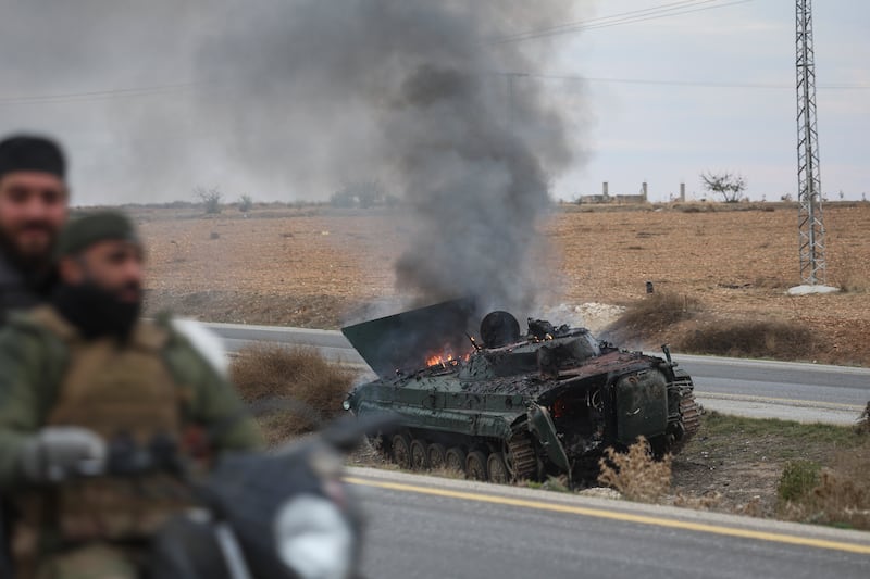 Syrian opposition fighters drive past a burning government armoured vehicle south of Hama (Ghaith Alsayed/AP)