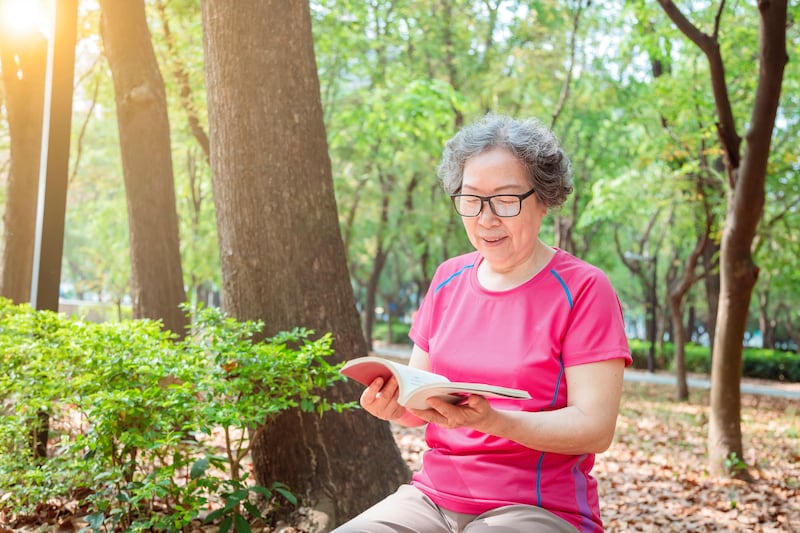 Senior woman in glasses reading a book in the park