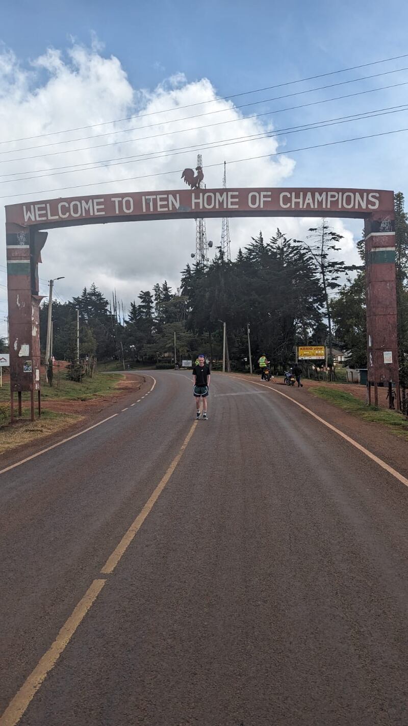 Zak Hanna poses beneath the famous 'Home of Champions' sign in Iten, Kenya