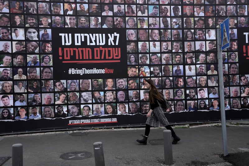 A woman in Jerusalem walks past photos of hostages held by Hamas in the Gaza Strip (Mahmoud Illean/AP)