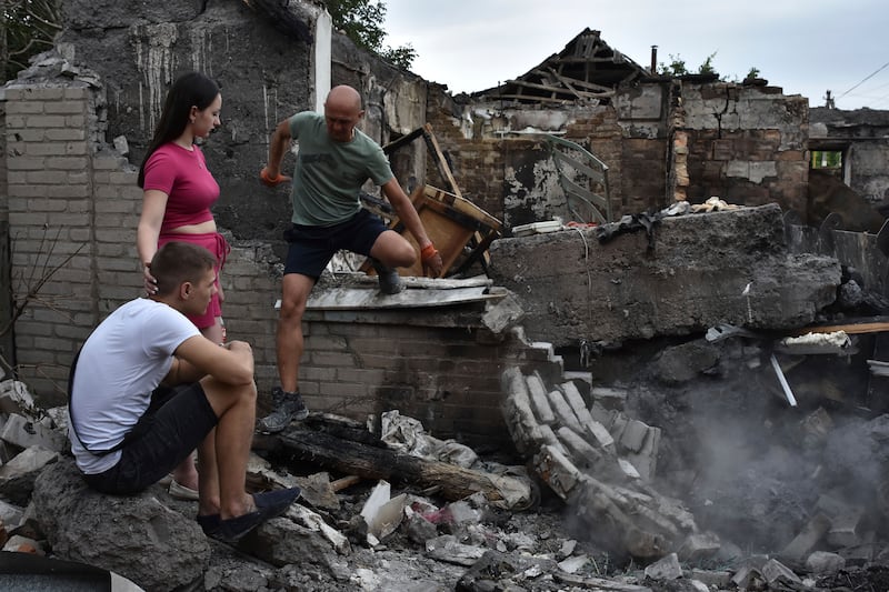 A family sit in front of their house destroyed by a Russian strike in Zaporizhzhia, Ukraine (Andriy Andriyenko/AP)