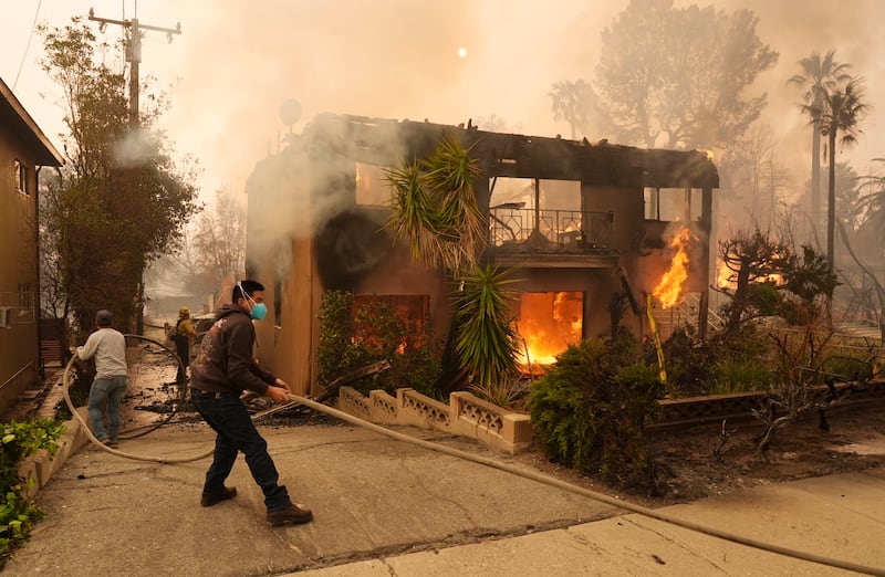 Pedestrians helped a firefighter stretch a hose as an apartment building burned in Pasadena (Chris Pizzello/AP)