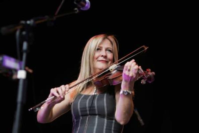 A photograph of Mairéad Ní Mhaonaigh playing the fiddle with a dark bagcround