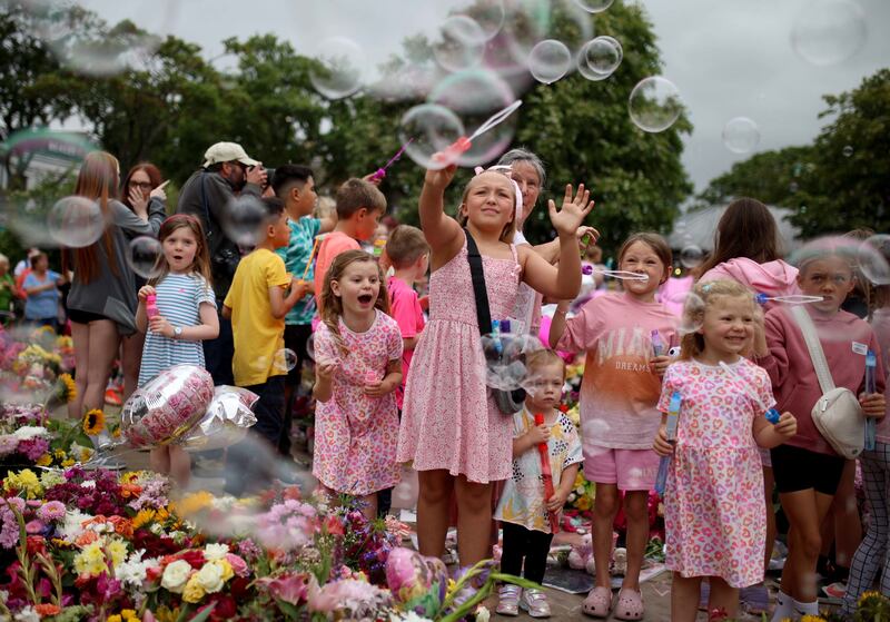 Young children play with bubble wands amongst floral tribute left outside the Town Hall in Southport