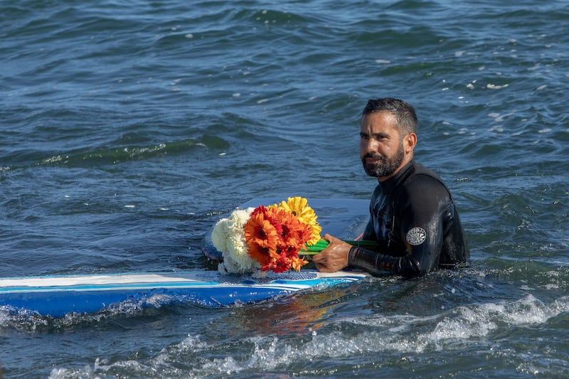 A man holds flowers during a tribute to 3 missing surfers (Karen Castaneda/AP)