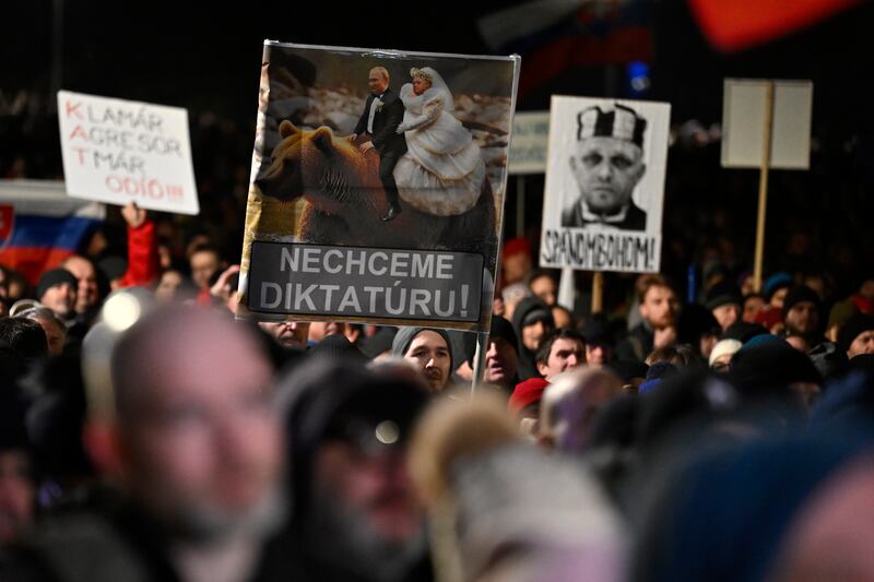 People hold up placards opposing Robert Fico (Denes Erdos/AP)