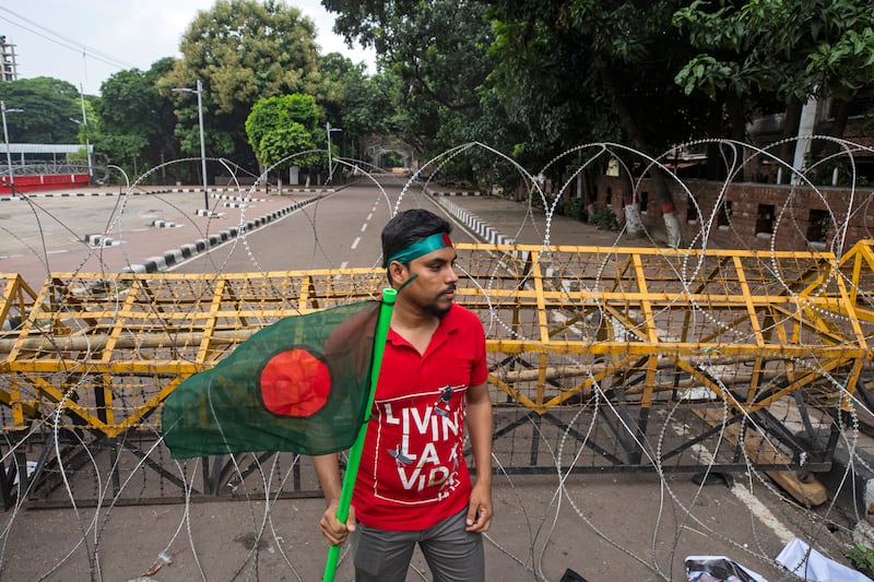 A protester carries the Bangladesh flag as he and others block the road in front of the former residence of Sheikh Mujibur Rahman