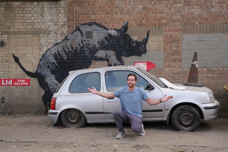 A man poses for a photograph by a new artwork unveiled by Banksy, depicting a rhinoceros