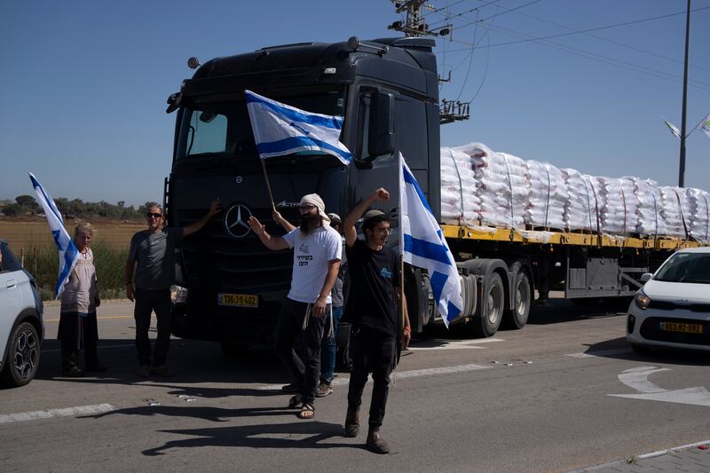 Holding Israeli flags people stand in front of lorries carrying humanitarian aid as they try to stop them to enter in the Gaza Strip in an area near the Kerem Shalom border crossing (Leo Correa/AP)